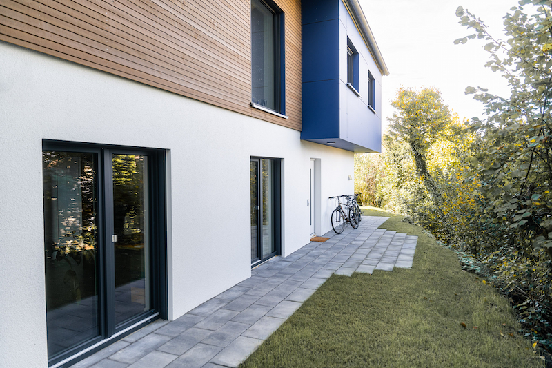 Ansicht der Gartenseite mit großformatigen Terrassentüren, weißer Putzfassade und Holzakzenten im Obergeschoss.