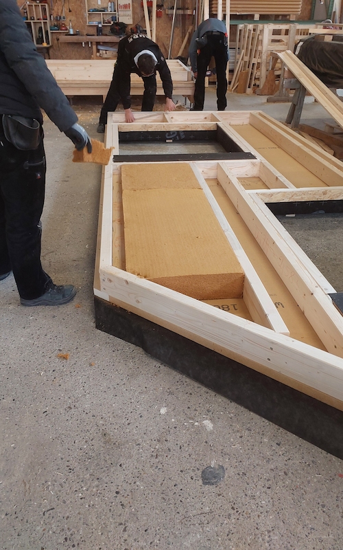 Handwerker montieren natürliche Holzfaserdämmung in ein Holzrahmenelement einer Wandkonstruktion.