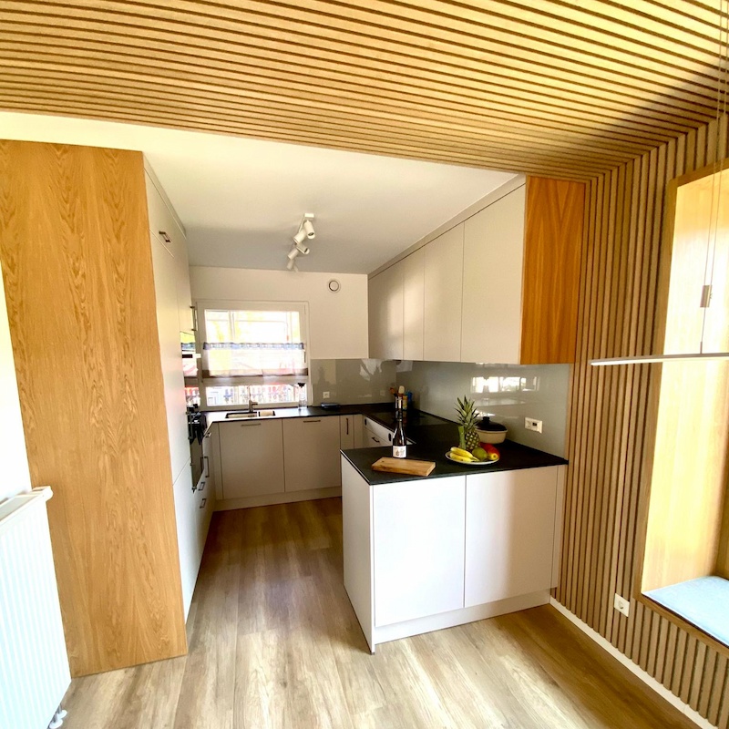 Moderne Einbauküche mit Holzdecke, heller Einrichtung und Kochinsel mit Obst und Wein.