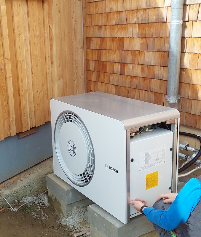 Installation einer modernen Bosch-Wärmepumpe an der Außenwand eines Holzhauses.